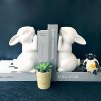 Serre-livres en céramique blanche en forme de lapins décoratifs maintenant des livres sur une étagère moderne