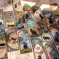 Set de 6 marque-pages en PVC avec illustrations de chats noirs et motifs vitraux colorés, sur fond bois