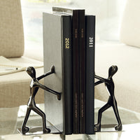 Serre-livre en métal noir représentant deux silhouettes poussant des livres sur une table

