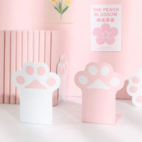 Serre-livre en métal rose et blanc en forme de patte de chat, posé sur une étagère rose