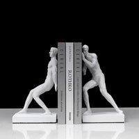 Serre-livre en résine blanche représentant deux silhouettes musclées tenant des livres entre elles.