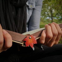 Marque-page en cuir en forme de feuille d’érable inséré dans un livre tenu en main