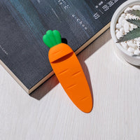 Marque page original en forme de carotte en silicone orange avec feuillage vert posé sur un livre
